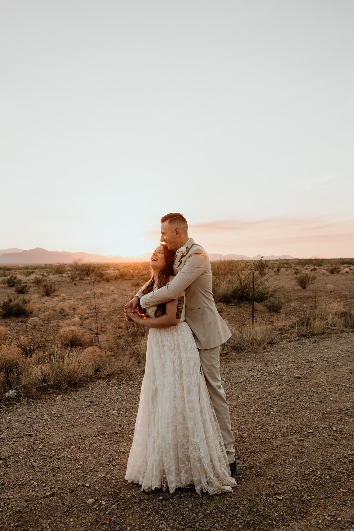 groom hugging bride from behind in the desert at sunset