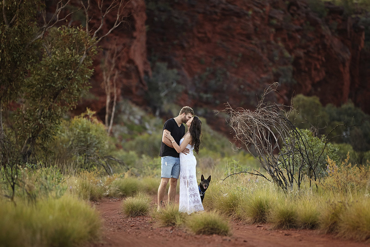 Couple kissing in natural rock location with dog hiding behind them