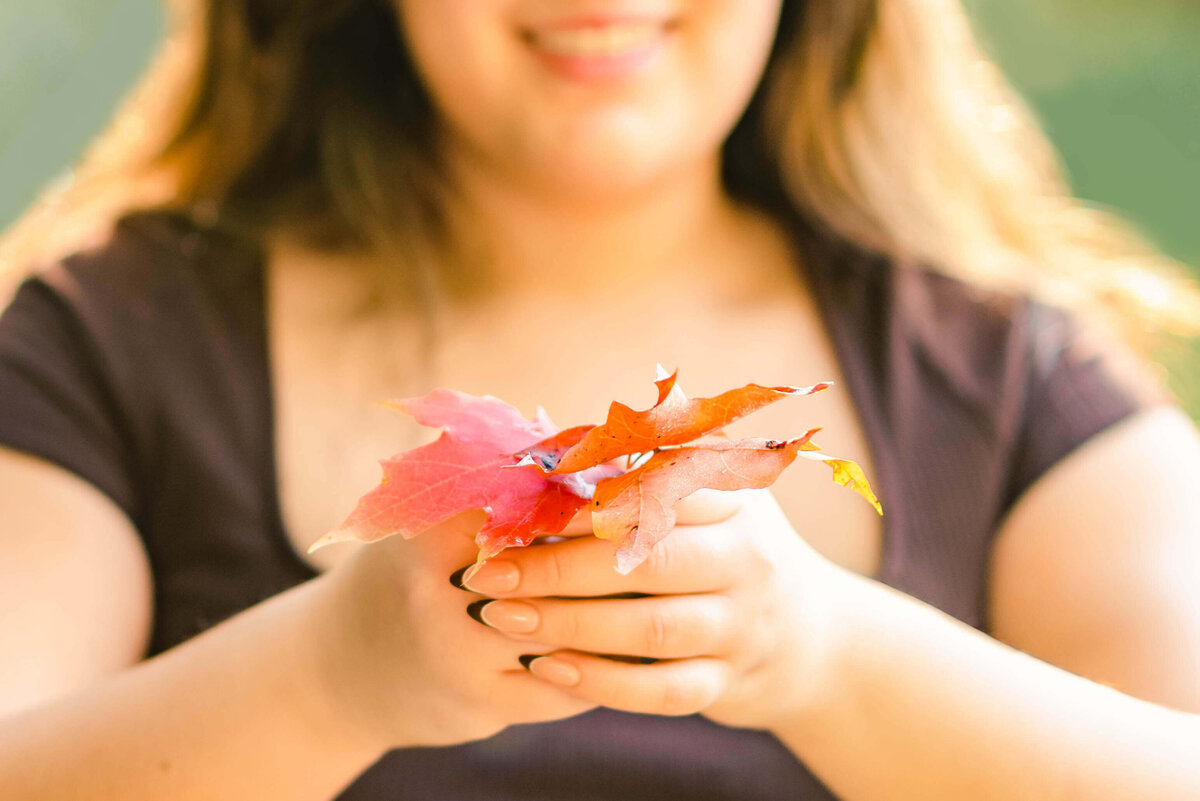 closeup shot of a high school senior holding out some red maple leaves