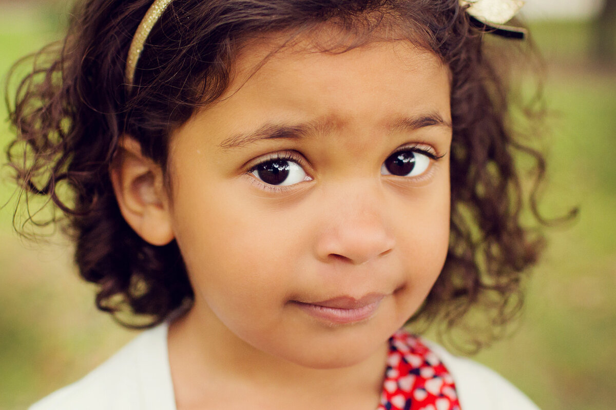 Close up photo of a little girl with dark, curly hair and huge brown eyes.