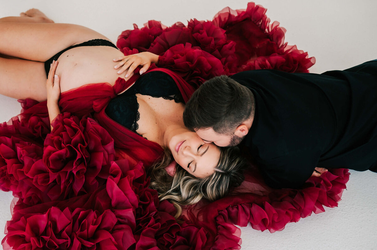 Springfield MO maternity photographer Jessica Kennedy of The XO Photography captures pregnant mom laying on floor kissed by husband