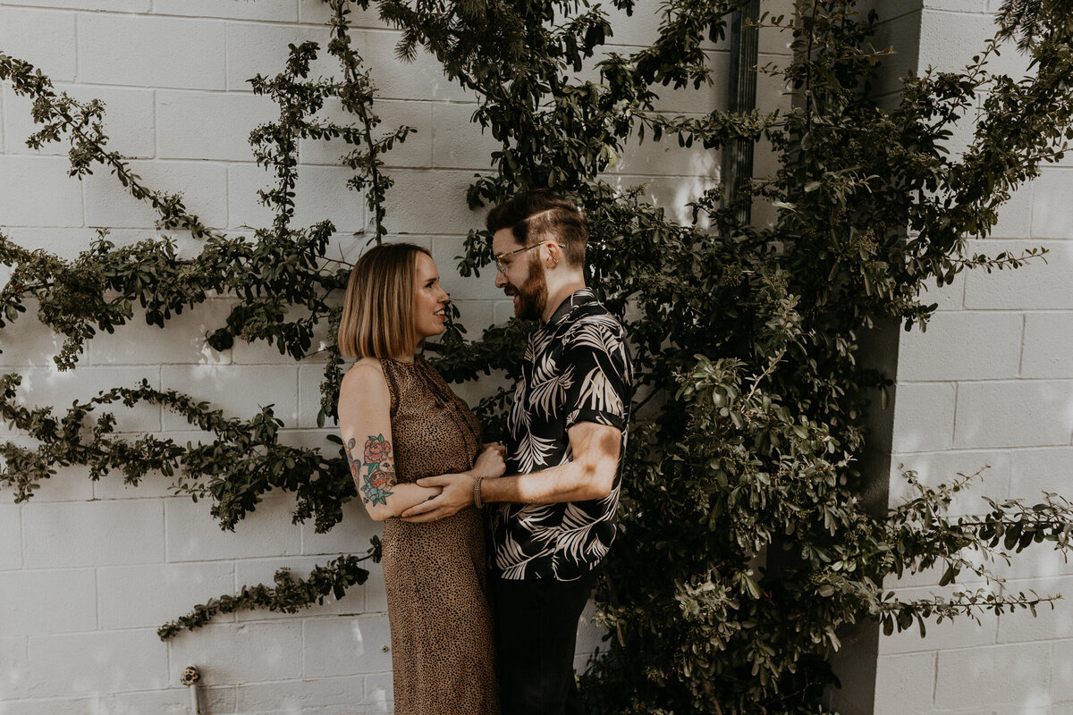 engaged couple looking at each other in front of a vine wall