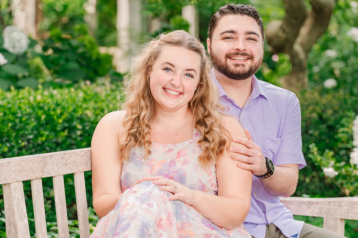 A happy couple sitting on a bench at The Arboretum in Raleigh for their engagement photos with JoLynn Photography, a Raleigh wedding photographer