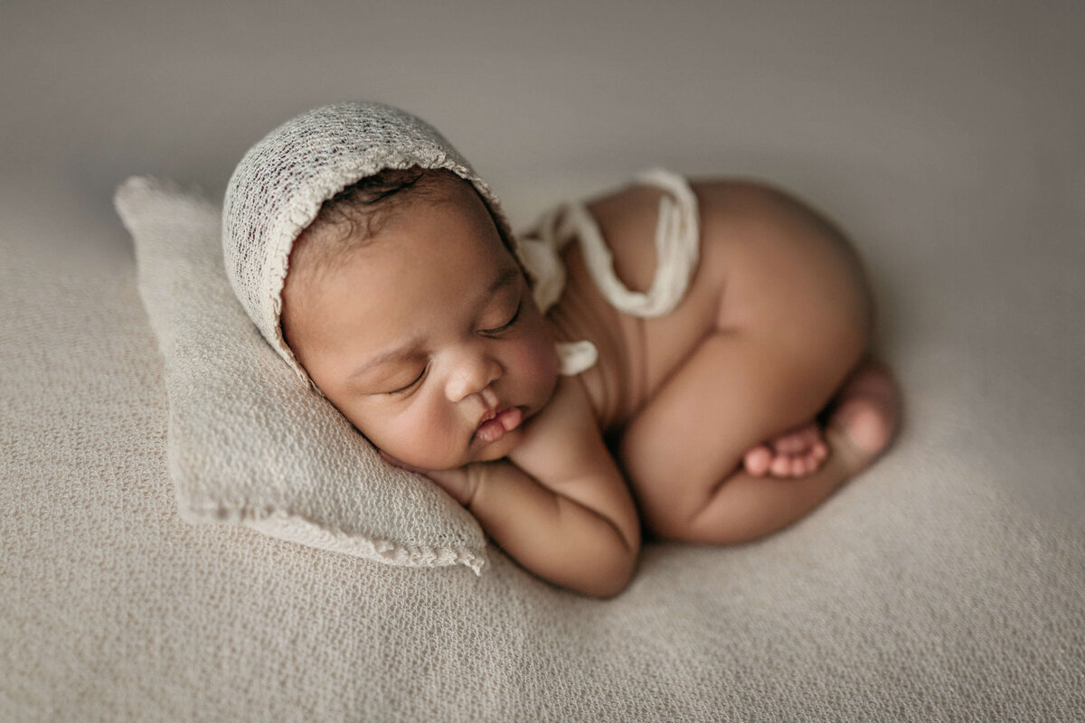 Newborn girl in tushie up pose with a bonnet laying on a pillow at a newborn photography session  in potomac falls va
