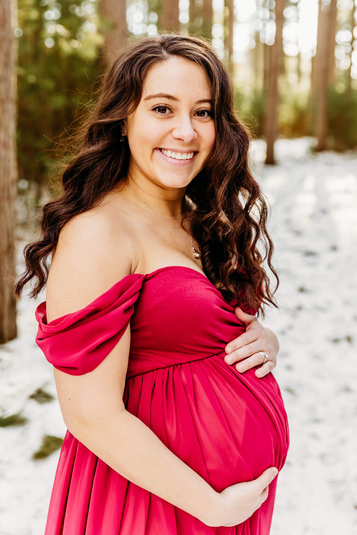 gorgeous pregnant mom smiling as she holds her baby bump during her winter maternity photo session