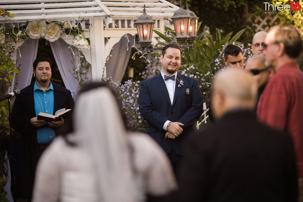 Groom waits at the altar as he smiles while his Bride is being escorted up the aisle
