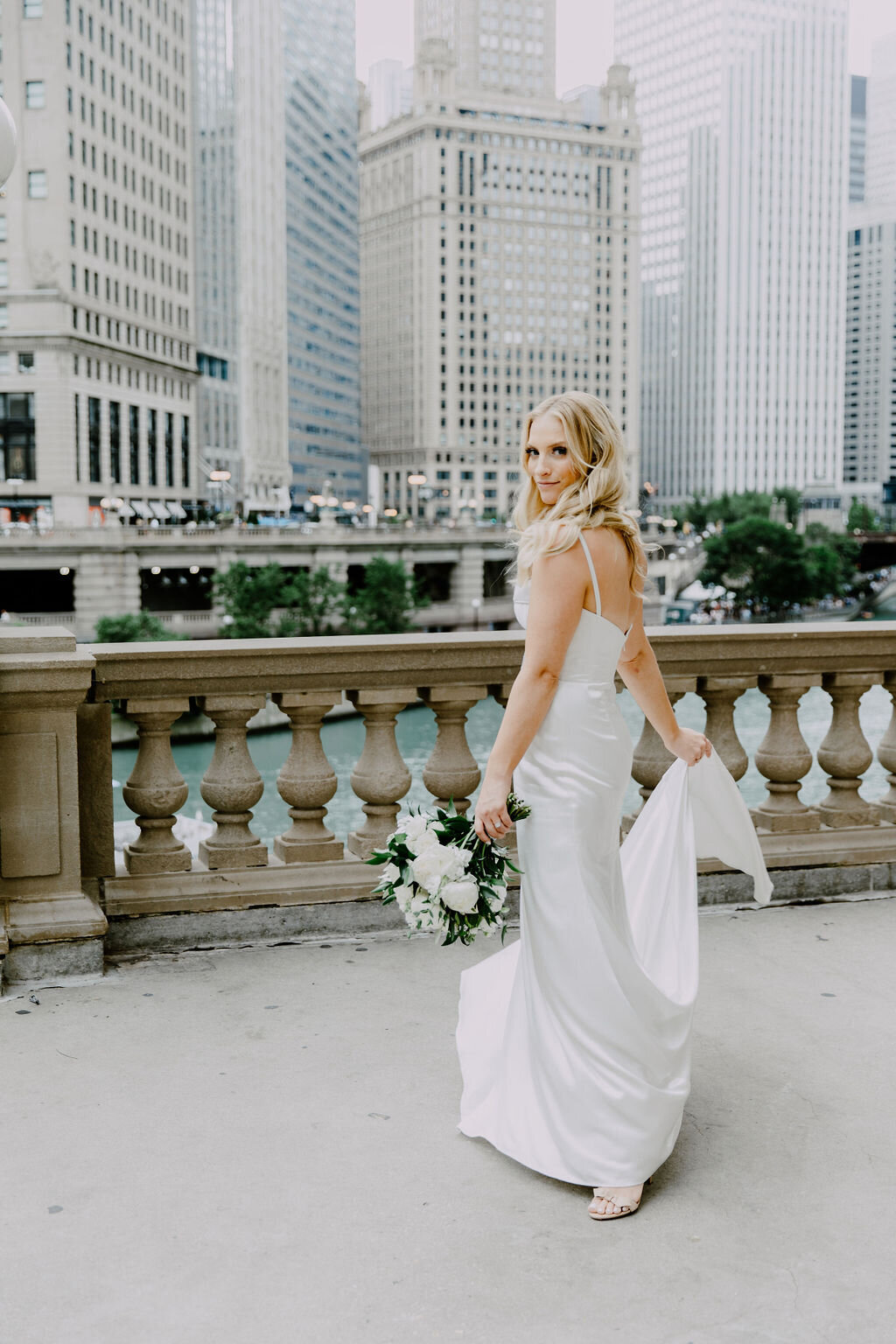 Elegant bride strolling through the vibrant streets of Chicago, her gown flowing gracefully, juxtaposed against the city's dynamic Wrigley Building's backdrop.