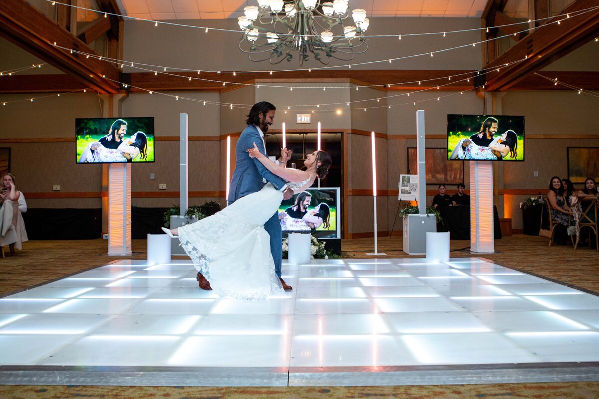 A groom lifts the bride in a dance pose on a lit-up dance floor with guests watching and two screens displaying the couple in the background at park farm winery weddings.