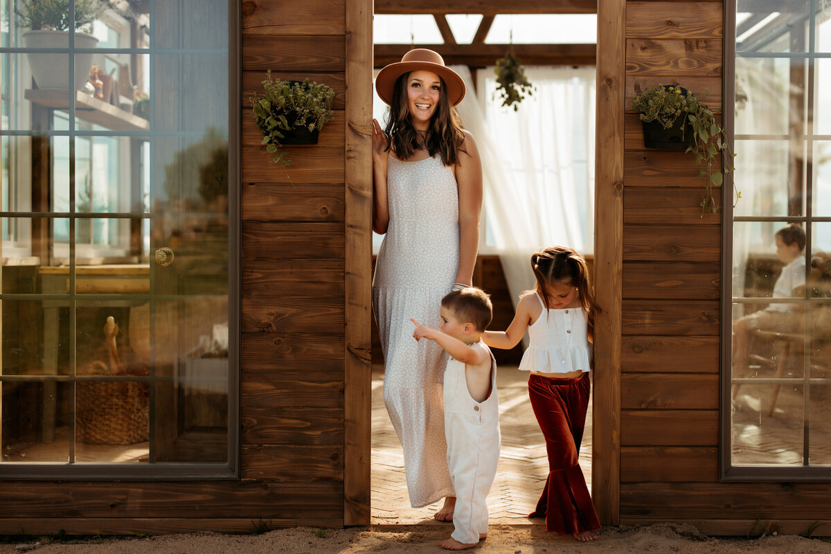 mom with two kids stand in door fram of wooden greenhouse