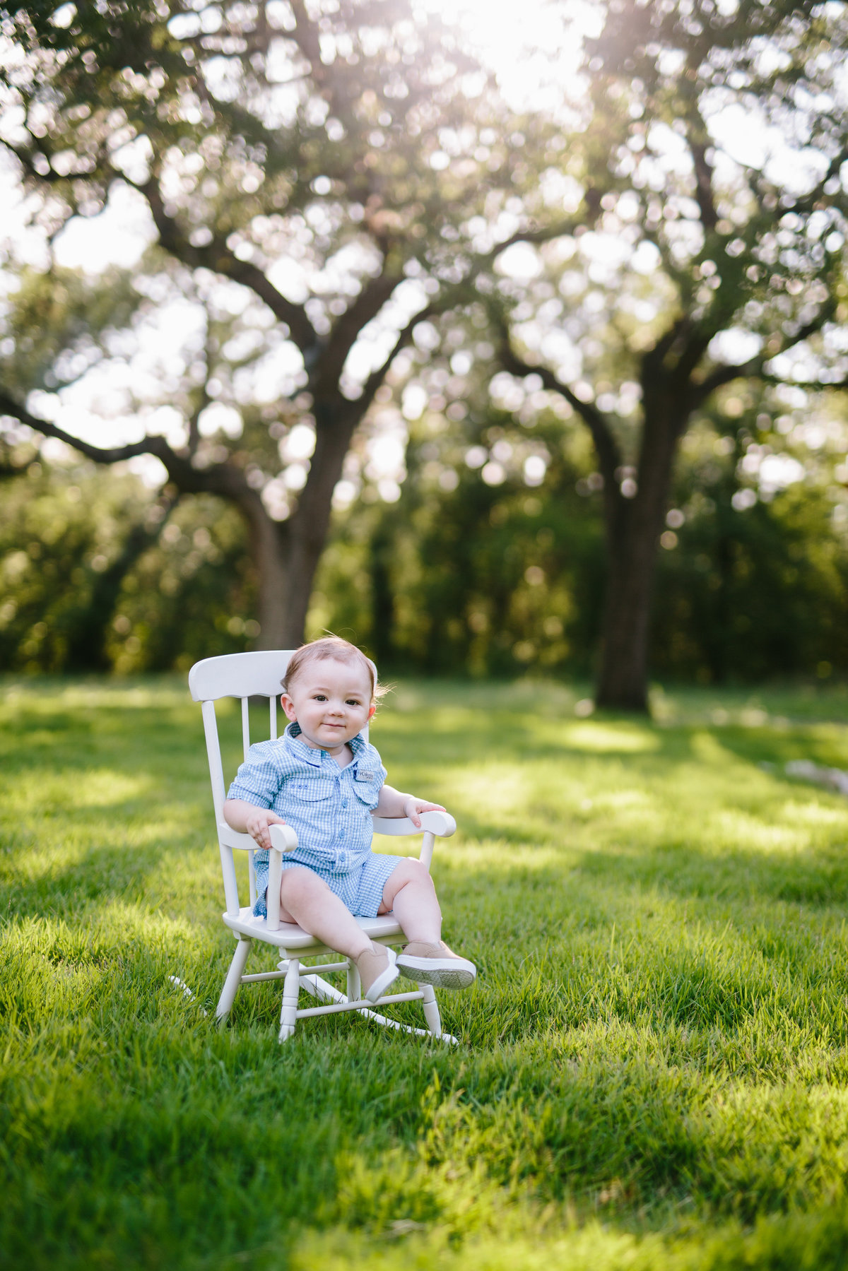 Photo of Baby toddler sitting in white rocking chair wearing blue jumper in forrest clearing at private San Antonio residence