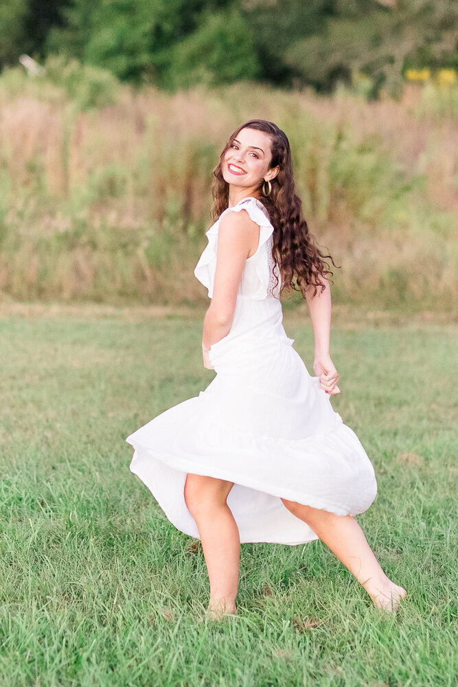High school senior girl in a white dress dancing in a field.