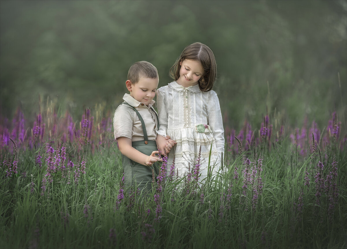 A young boy and his older sister hold hands and observe the lilac plants around them. Located in Ottawa.