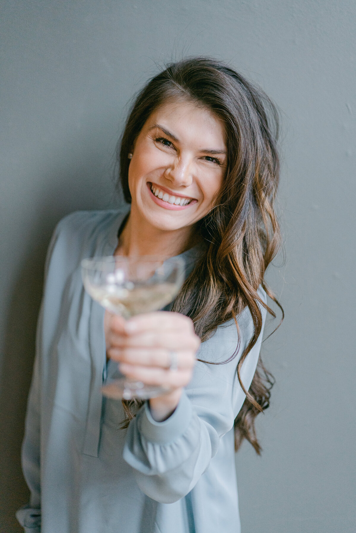 a woman with a champagne glass  in her hand extending it towards the camera for a toast