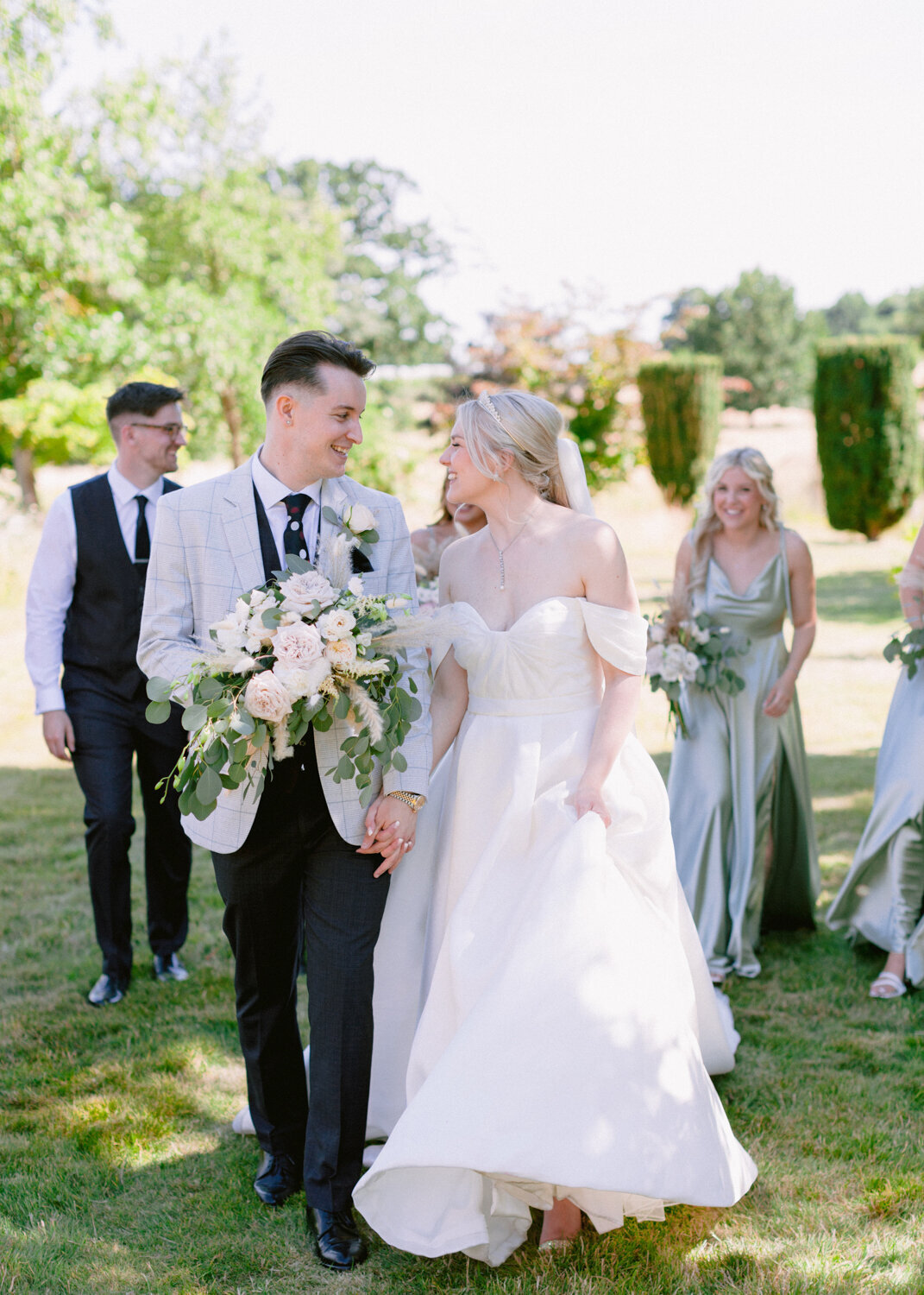 bride and groom walking next to each other with bridesmaids and groomsmen following behind