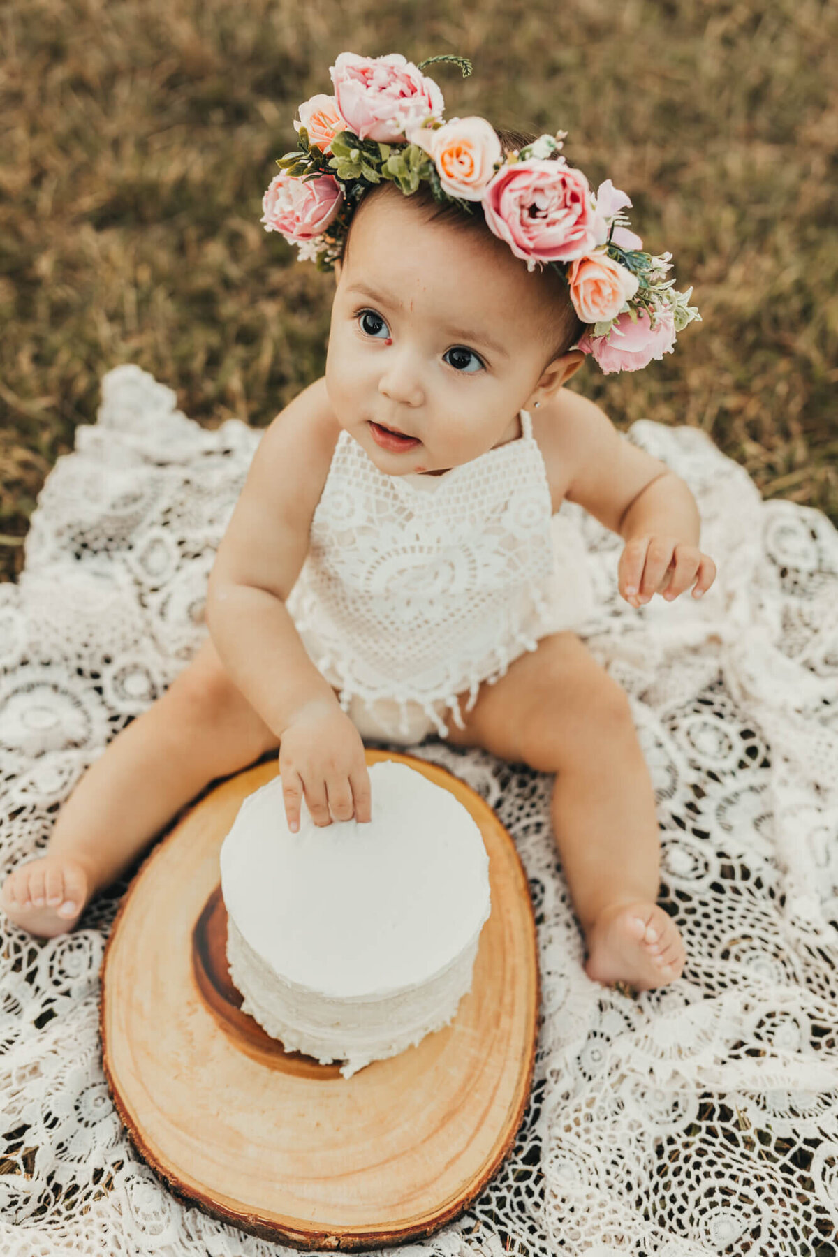 celebrating her birthday, little girl wears white romper and digs into cake.
