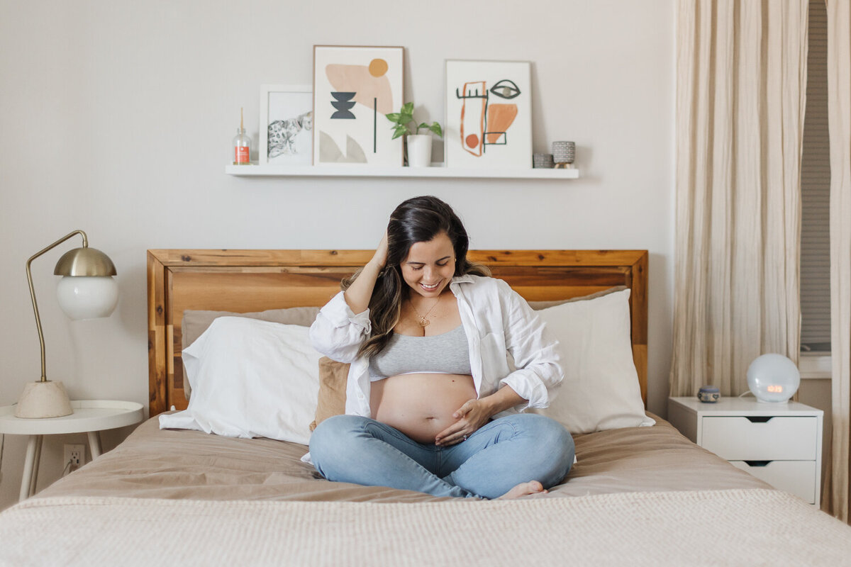 Expecting mama sitting on bed during her at home maternity photography session in her toronto home