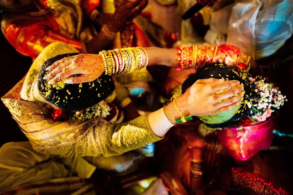 An intricate top-down view of a traditional South Asian wedding ritual, hands adorned with henna and richly colored attire.
