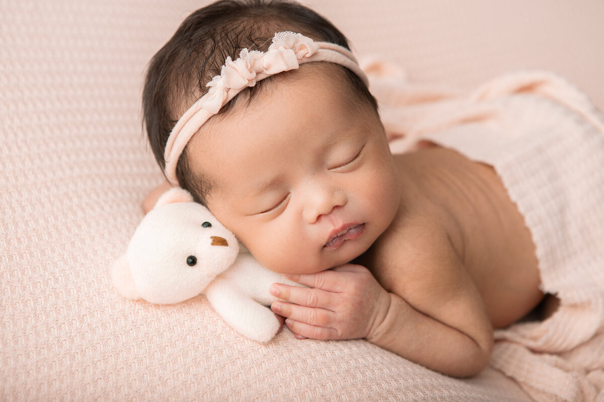 Newborn studio table pose on a pink backdrop with a white teddy bear