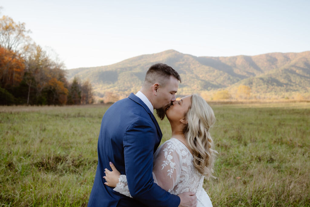 Cades Cove elopement with bride and groom kissing as they elope to Gatlinburg with a field and mountains in the distance captured by Gatlinburg photographer 