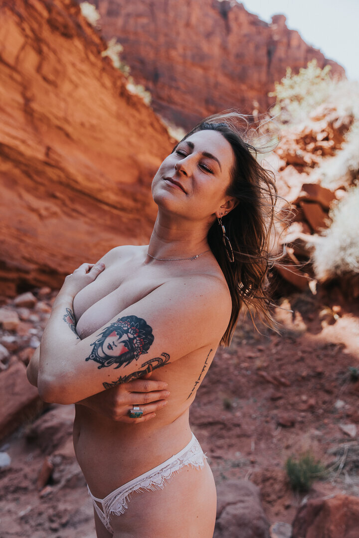 A woman standing topless in a Moab canyon with the wind in her hair.