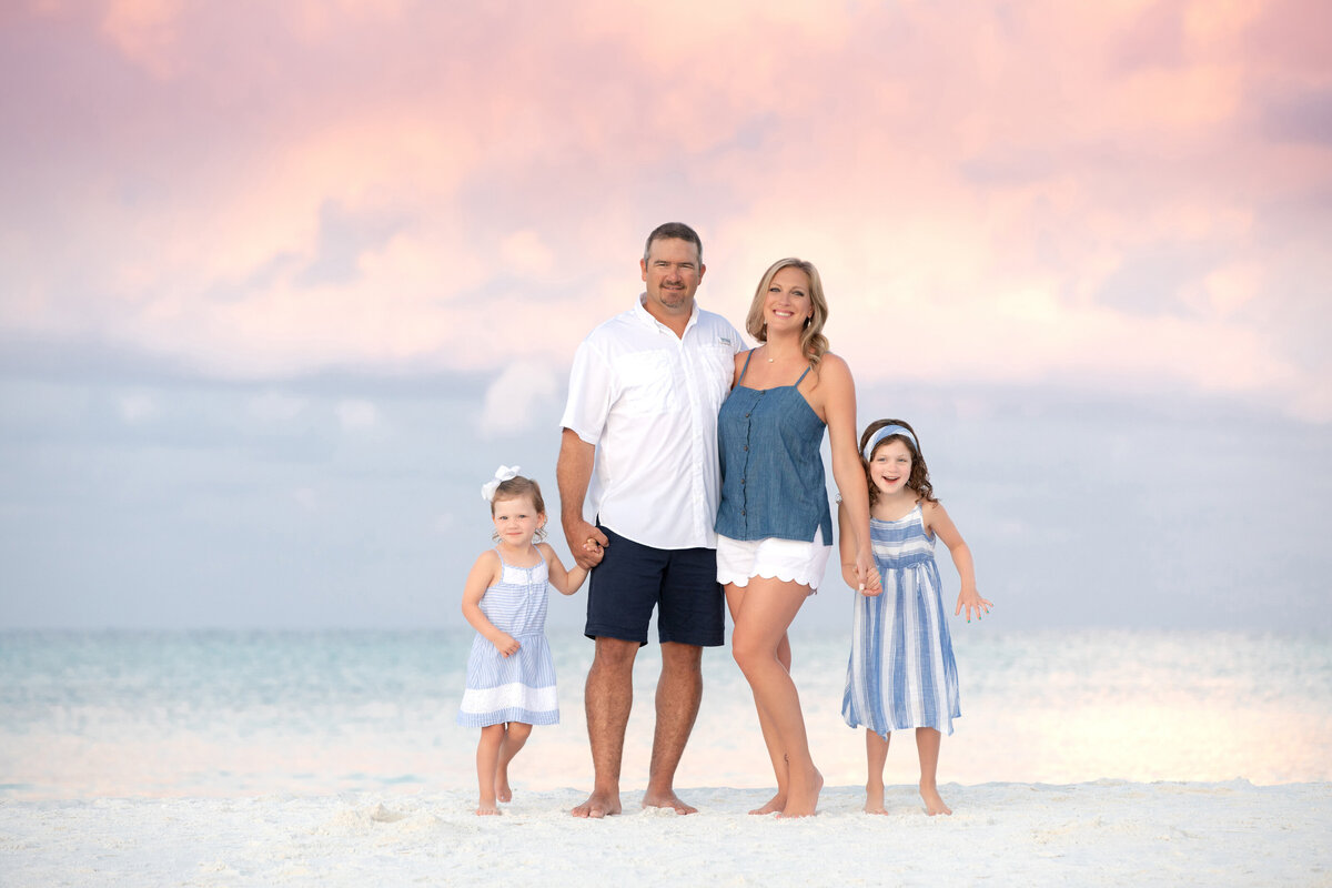 Two parents each holding a child's hand at the beach