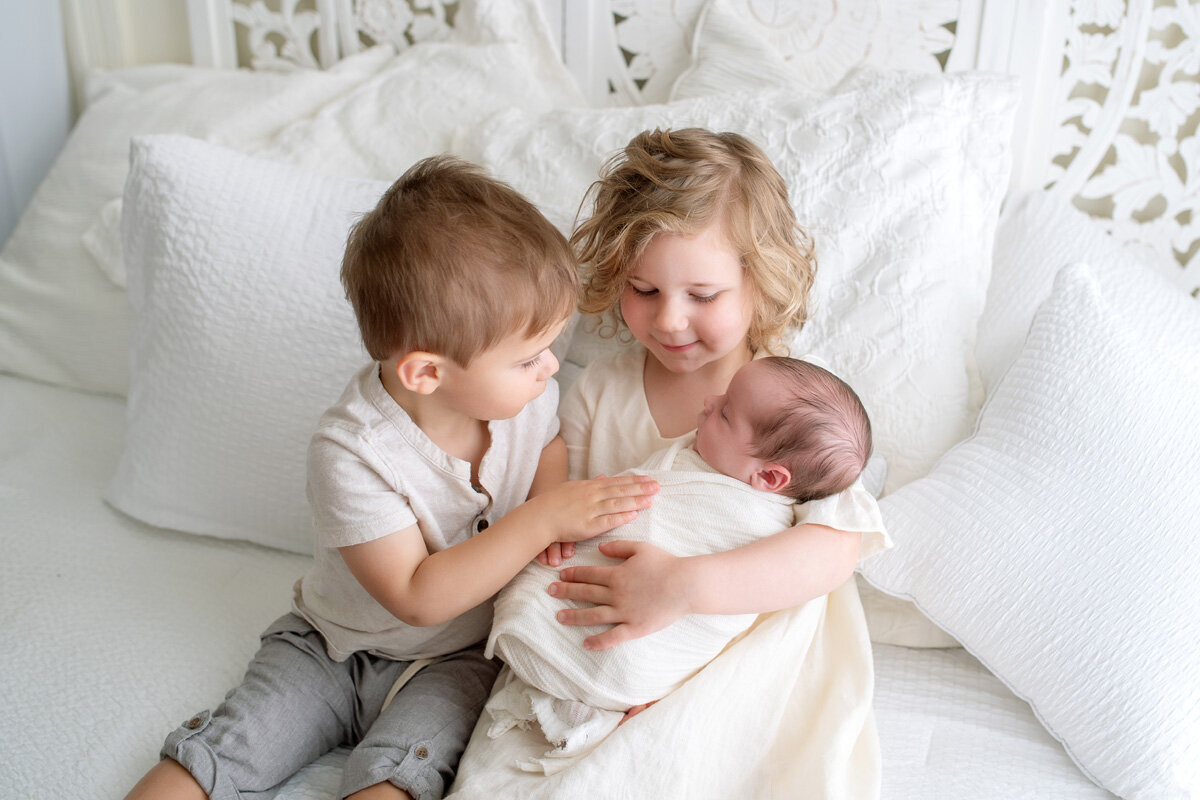 Newborn session with two older siblings sitting on the bed