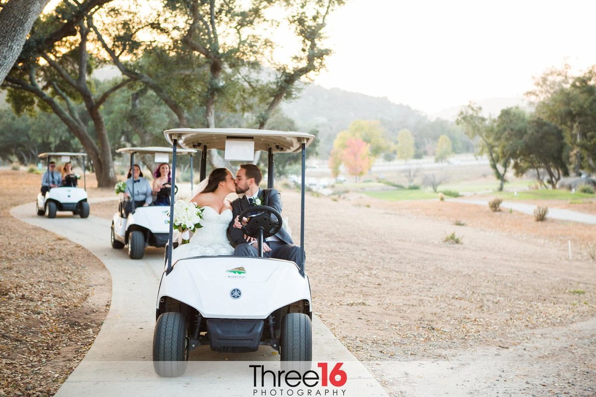 Bride and Groom kiss in golf cart in front of bridal party