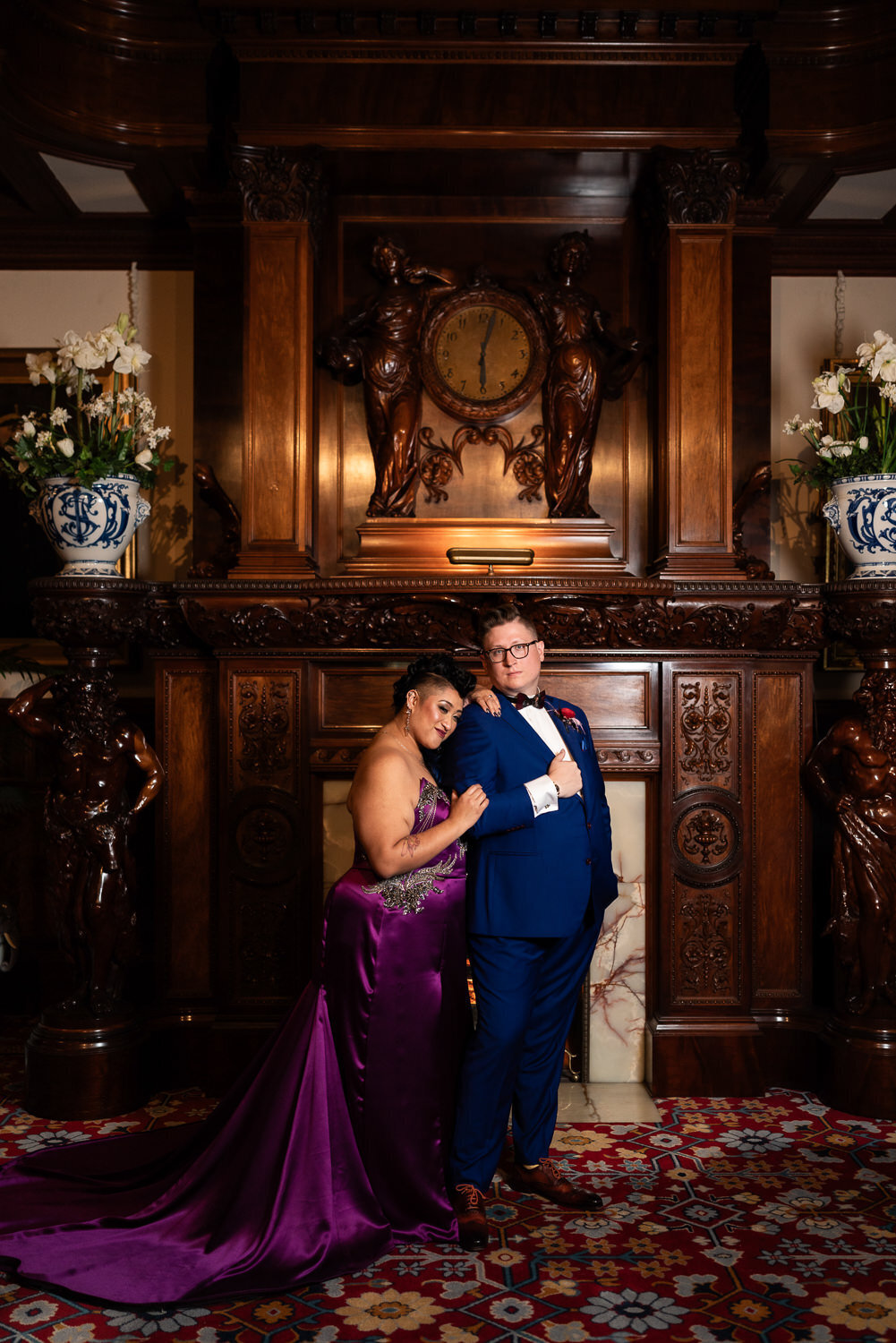 Filipino bride in purple dress and groom smile in front of a fireplace.