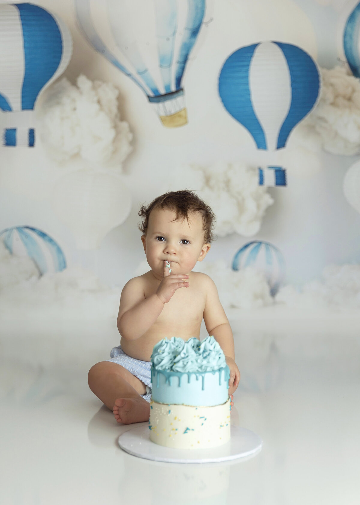 A young toddler holds up a cake covered finger during his session with a New Jersey Cake Smash Photographer