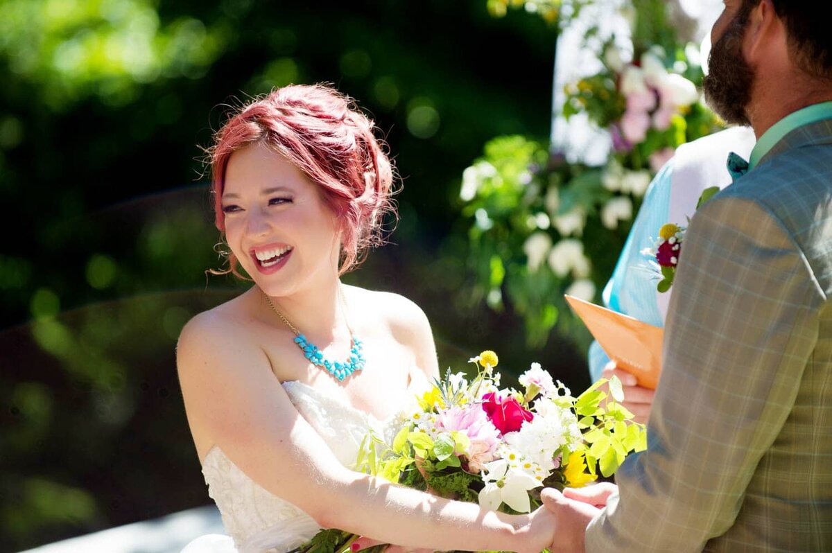 a pretty bride with red hair laughs at the guests during the wedding vows