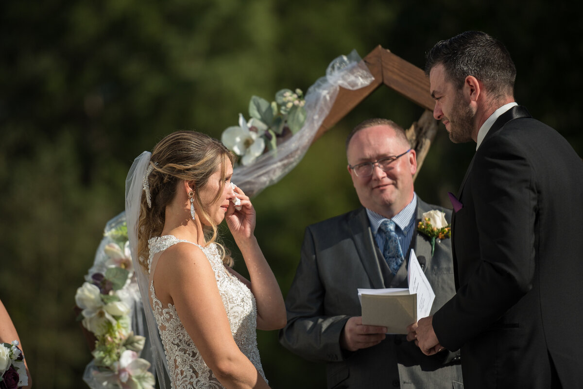 Bride crying during wedding vows with pastor in background.