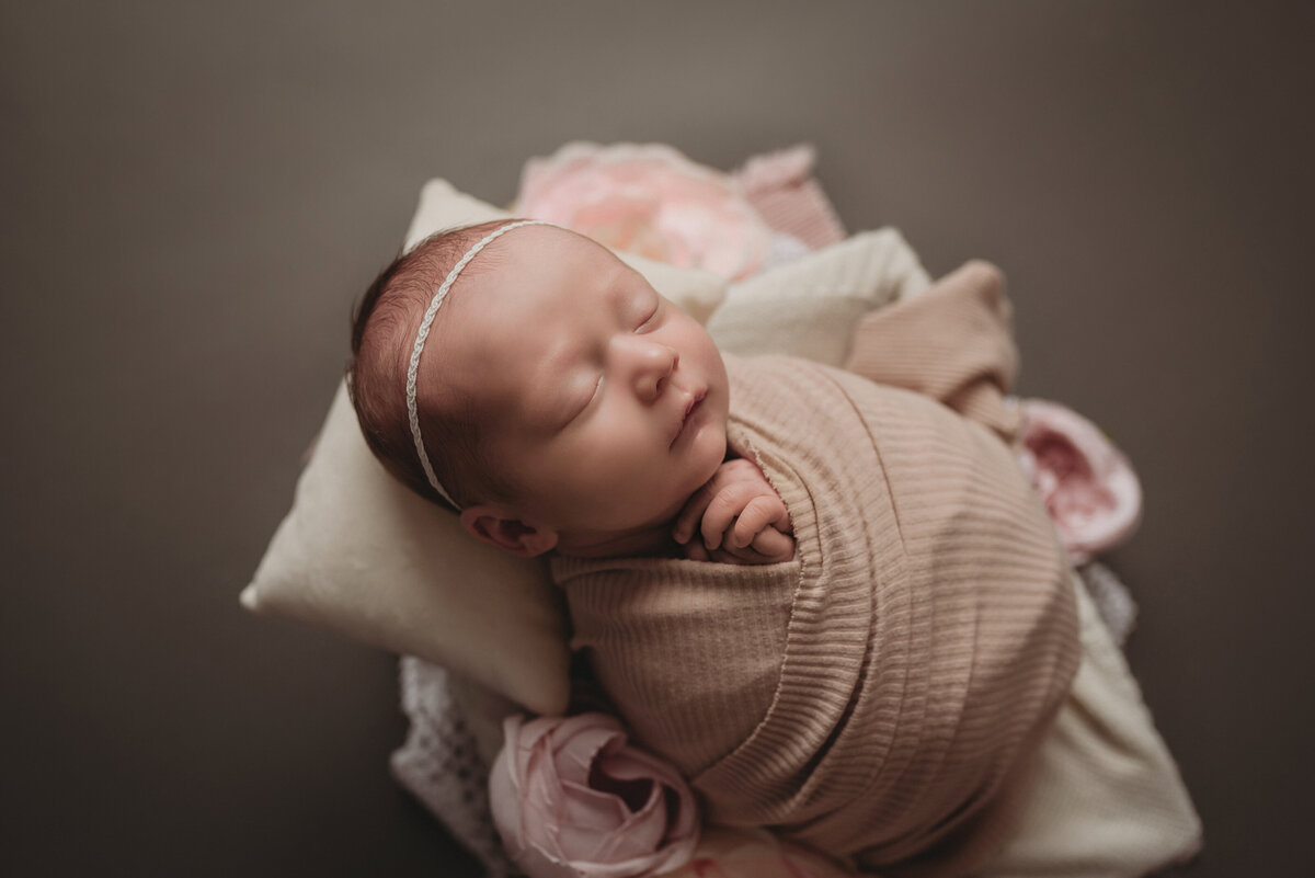 Sleeping newborn girl at newborn photo shoot in marietta, ga wrapped in pink swaddle laying in lace and roses on dark gray backdrop