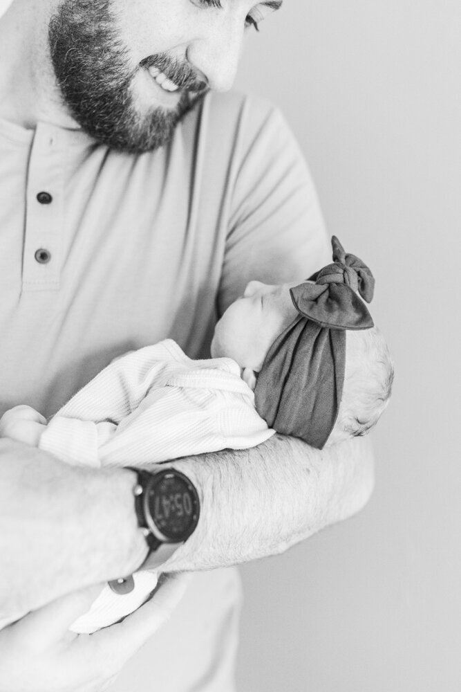 a dad smiling while holding his newborn baby