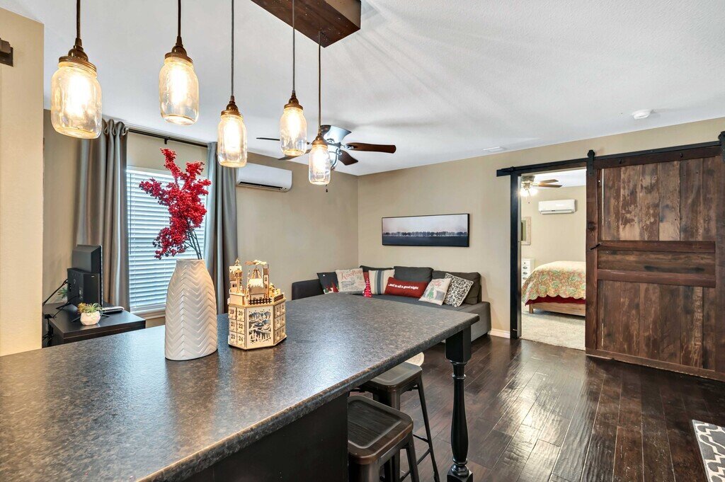 Kitchen island with open concept living room and barn door opening to bedroom in this four-bedroom, four-bathroom vacation rental home and guest house with free WiFi, fully equipped kitchen, firepit and room for 10 in Waco, TX.