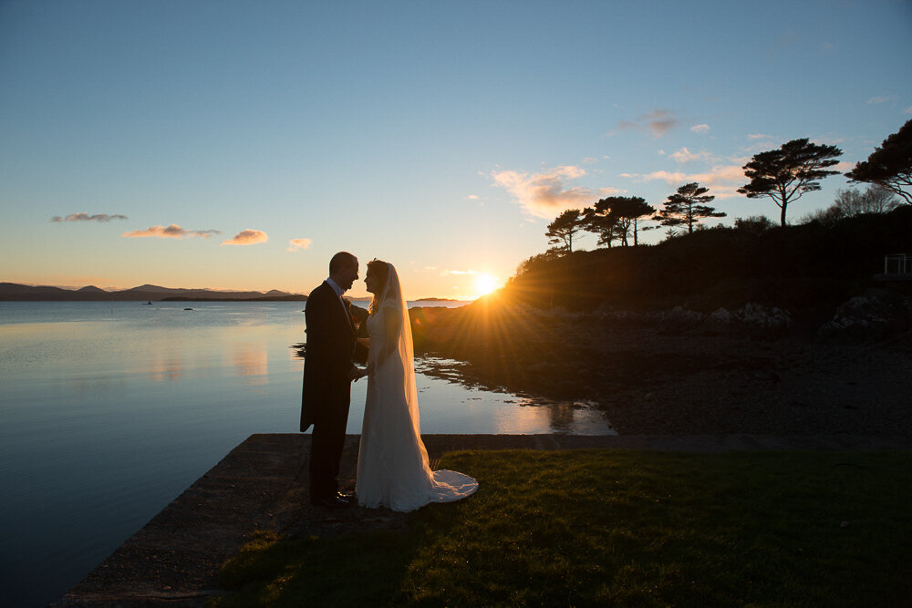 silhouette of bride and groom standing on the edge of a pier at the Parknasilla Hotel, Kenmare with the sun setting in the background