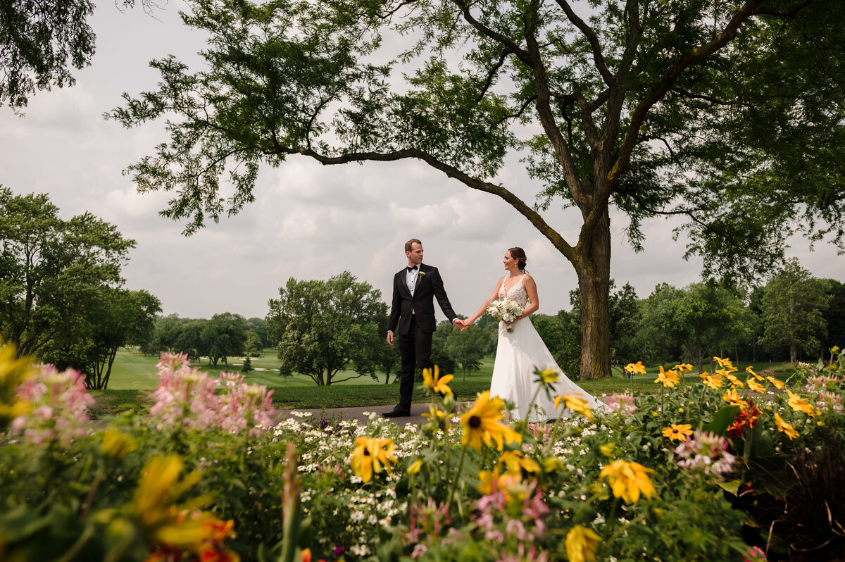 Bride and groom hold hands behind flowers at Biltmore Country Club in Barringhton, IL