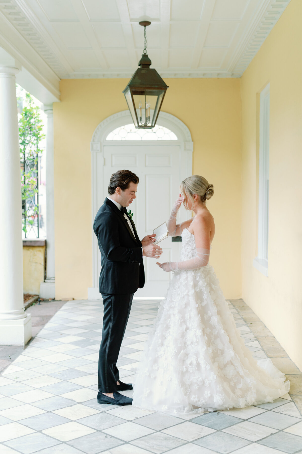 Emotional private vow reading at the piazza of William Aiken House. Marble checkered floors and gas lantern at historic Charleston wedding venue with yellow walls. Charleston wedding photographer.