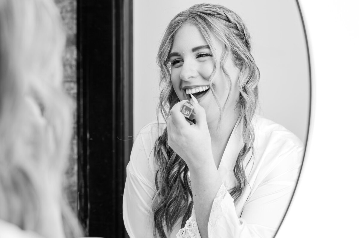 A happy blonde bride putting on lipstick in the mirror at The Orpheum on her wedding dy by JoLynn Photography, a Raleigh wedding photographer
