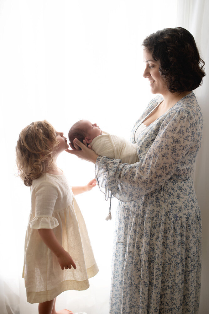 Newborn session with older sister and mother wearing a dress