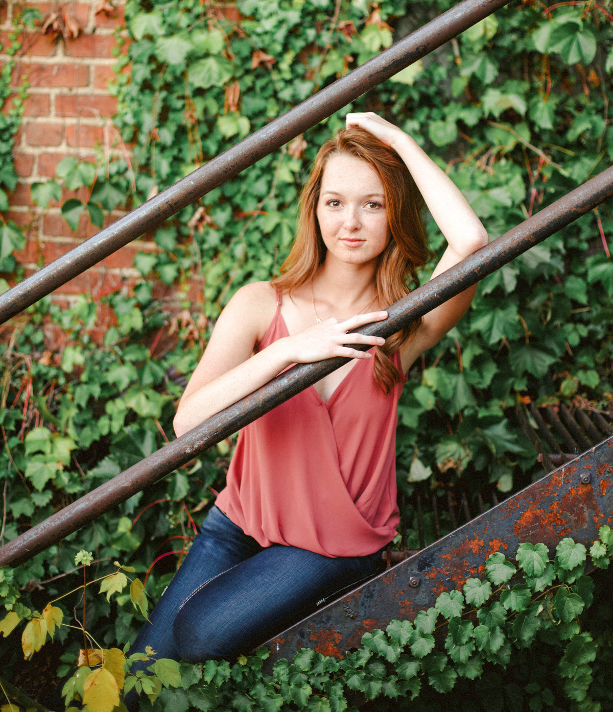 senior girl sits on rusted staircase outside building of ivy and brick