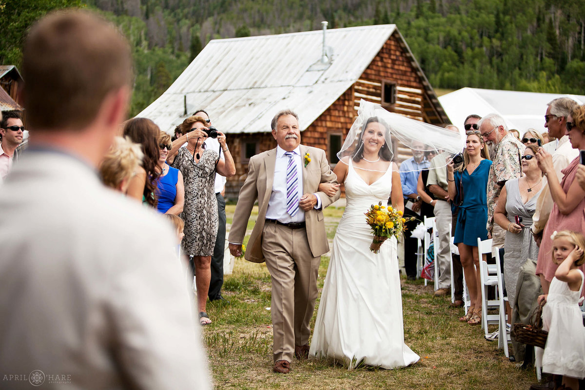 Bride walks down the aisle with her dad at Catamount Ranch barn in Steamboat Springs