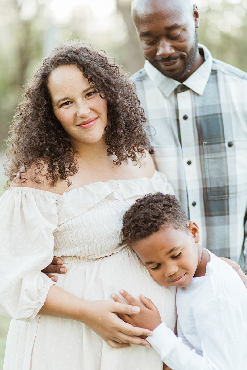10 year old black son hugs his moms’ pregnant belly while dad watches