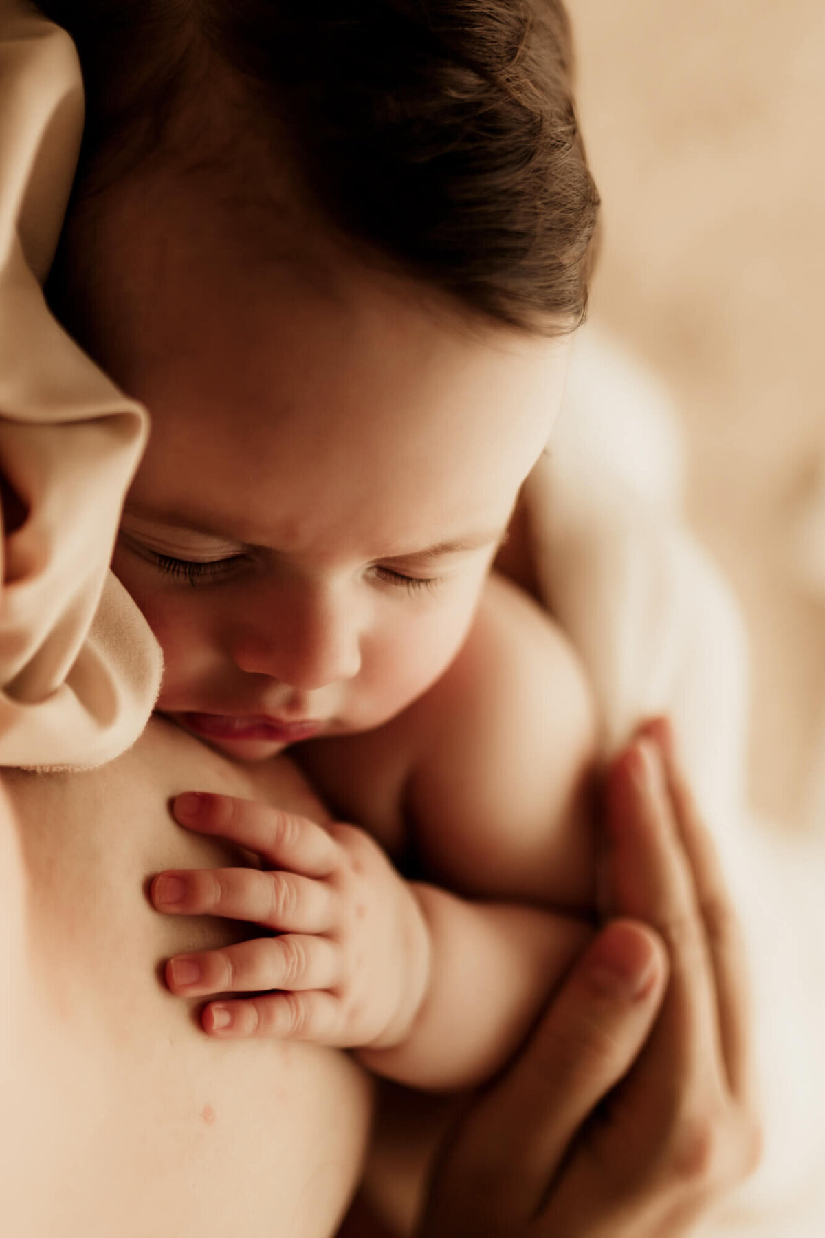 Sleeping baby girl with dark brown hair resting her hand on her mother.