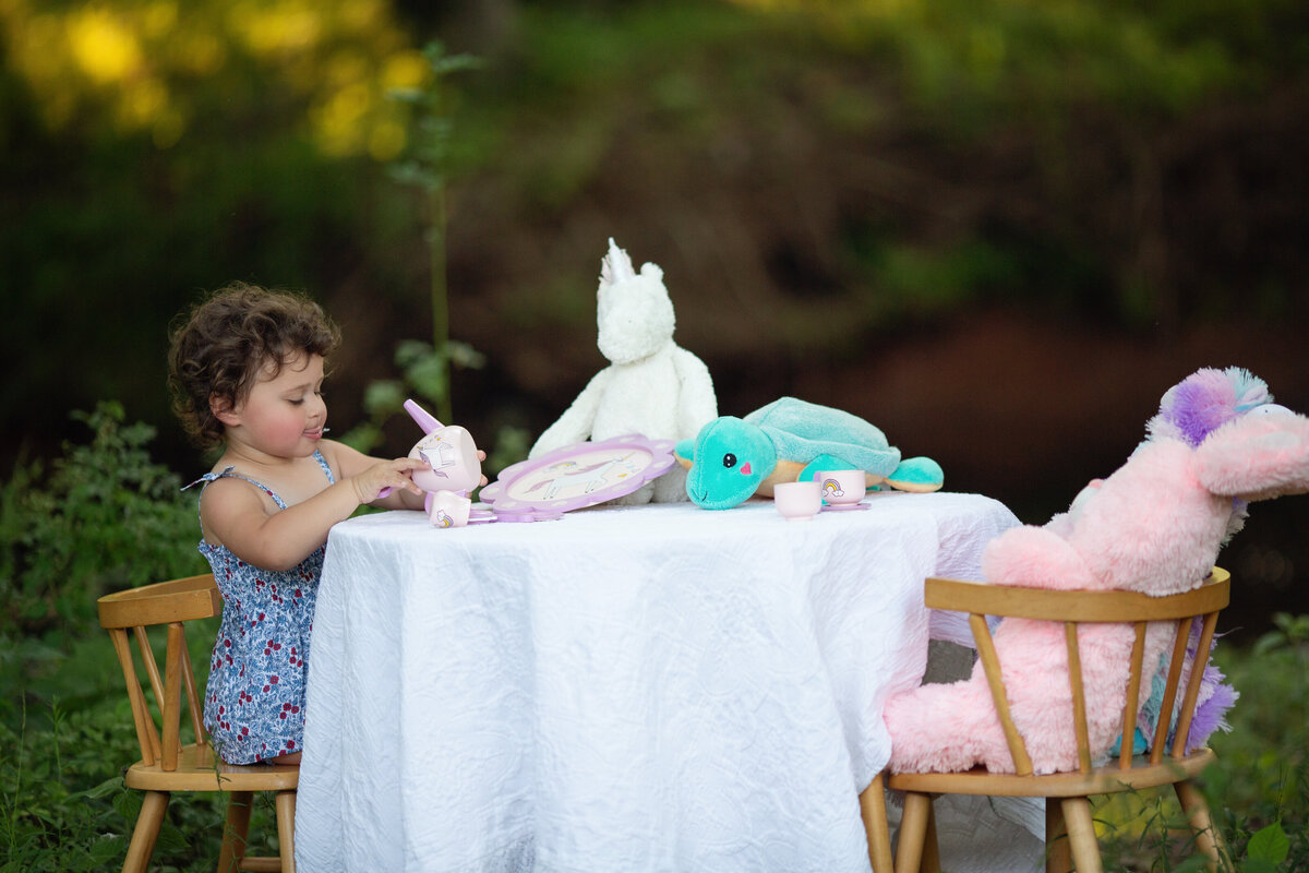 A toddler girl has a tea party in a park with her favorite stuffed animals