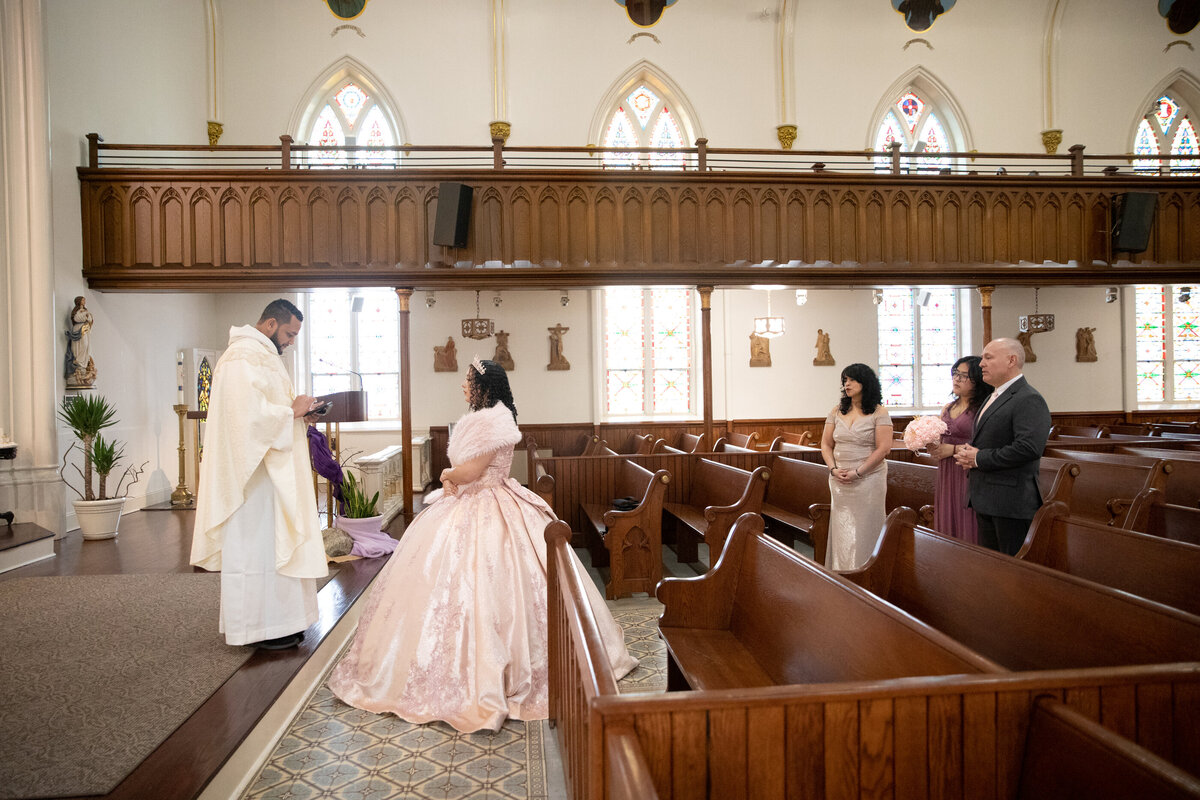 priest blesses young Mexican-American teenage girl in crown and ballgown with her family Saint Peter's Church Haverstraw quinceanera photographer Rockland County Milestone Images