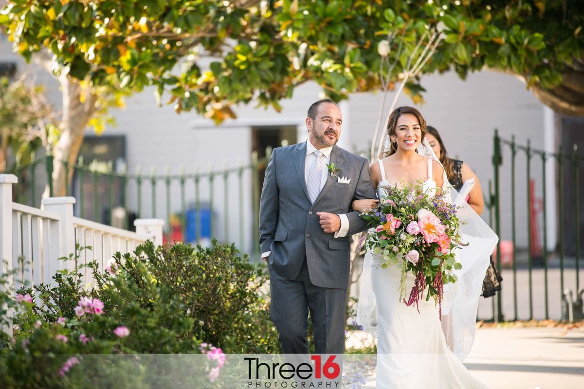 Bride has a big smile as her father escorts her towards the aisle at her wedding ceremony