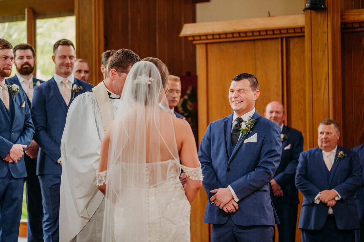 photo of a groom in a navy suit winking at the bride