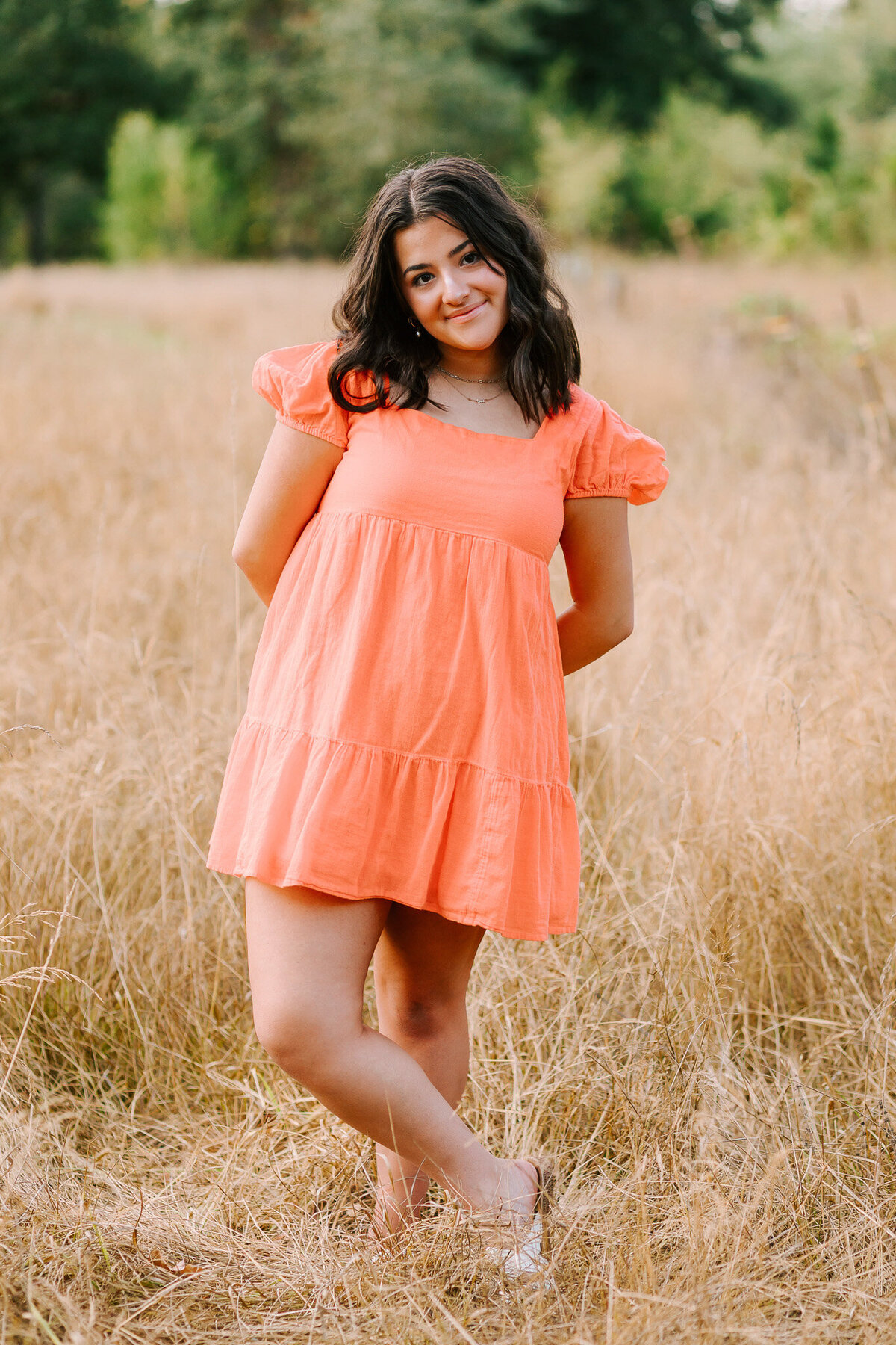 A high school senior in a coral dress stands in a coral dress in a field in Albany