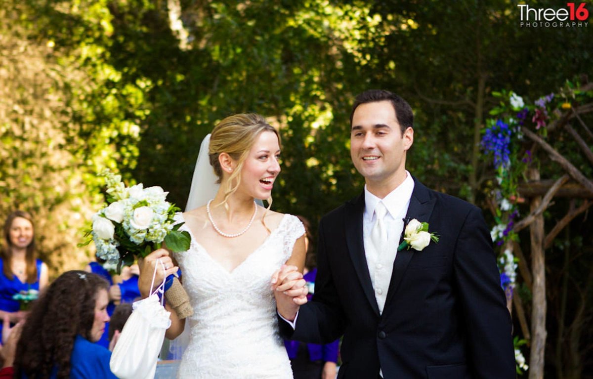 Bride and Groom walk down the aisle together holding hands and smiling