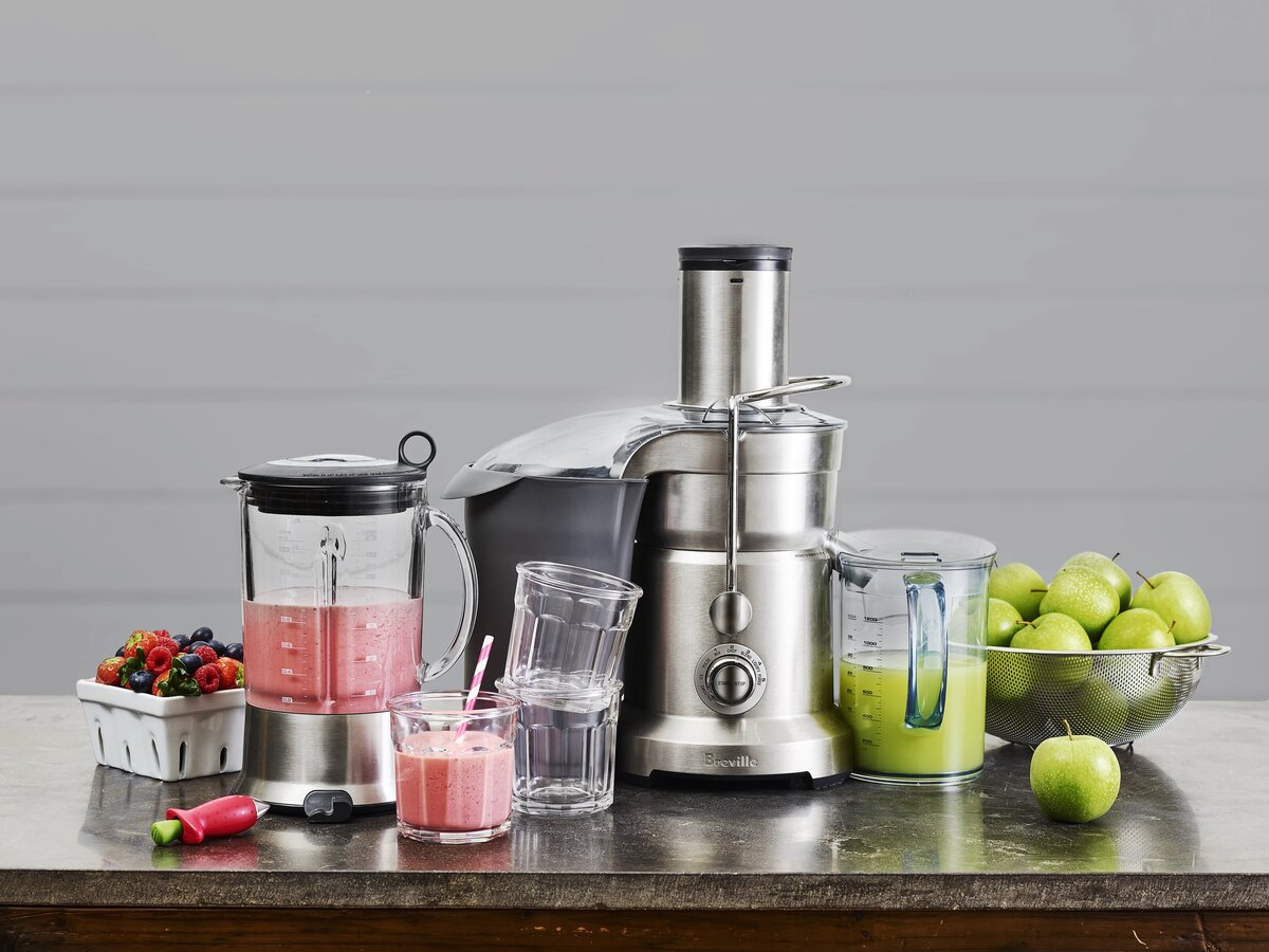 A juicer on a counter with apples and berries next to it.